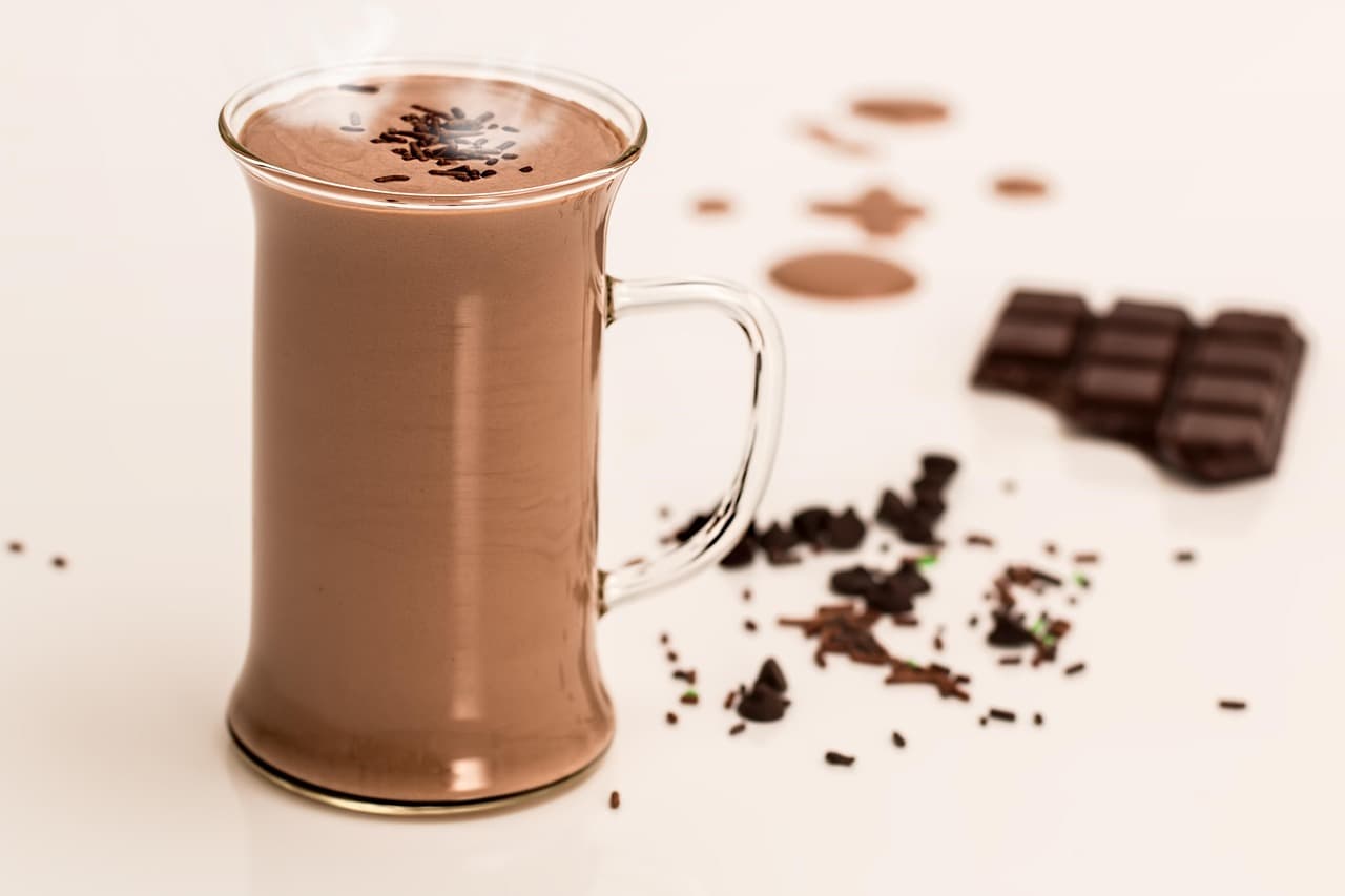 A tall glass mug of hot chocolate beside squares of chocolate