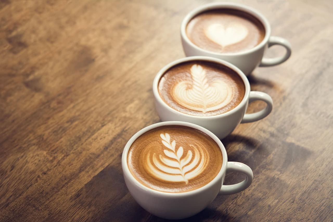 Three lattes with leaf and heart latte art on a wooden table