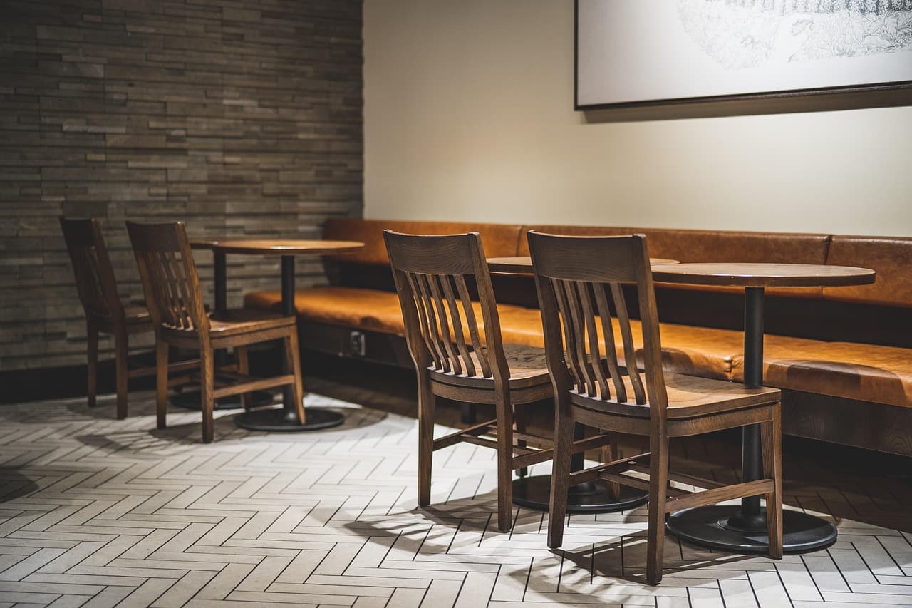 A quiet cafe with wooden tables and chairs and a bench along a brick wall