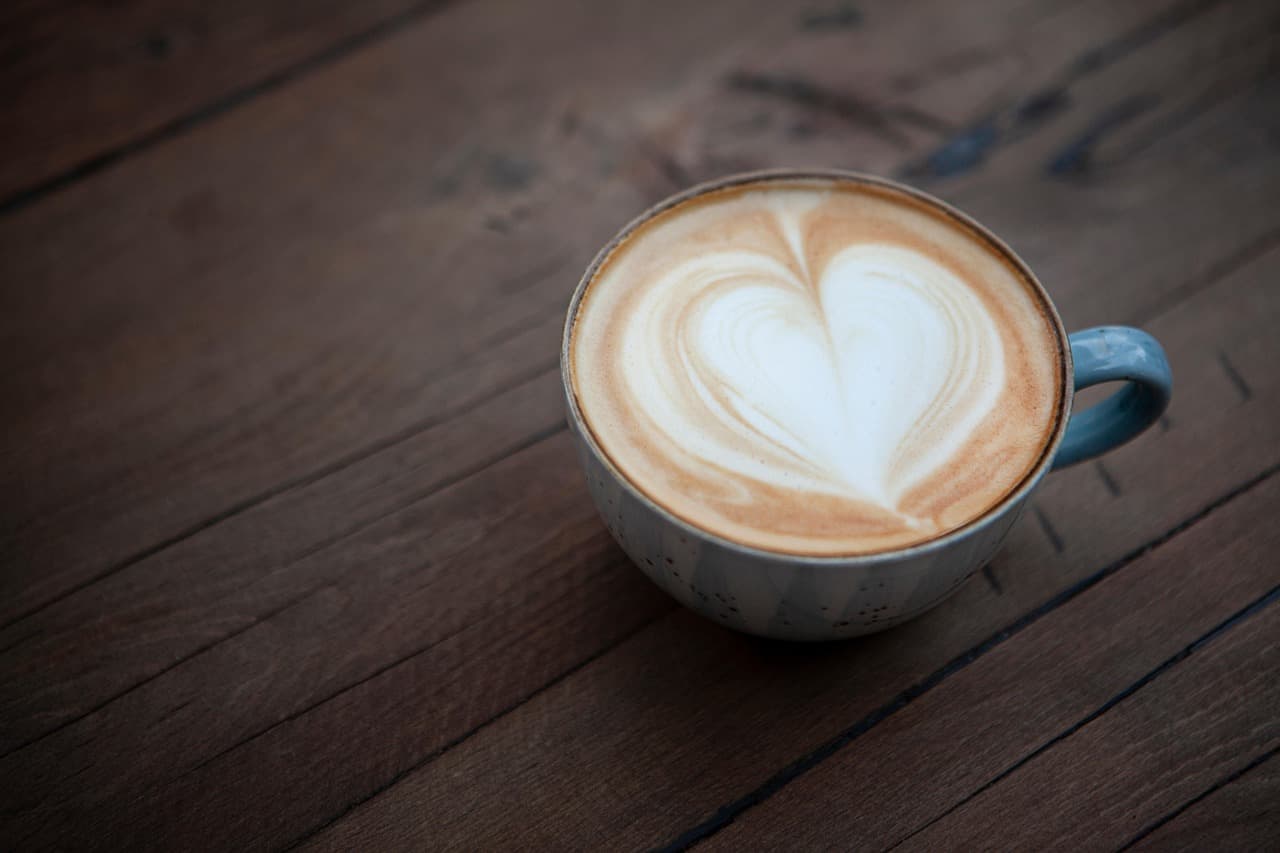 A latte with a heart in the foam, in a cup with a blue handle on a wooden table